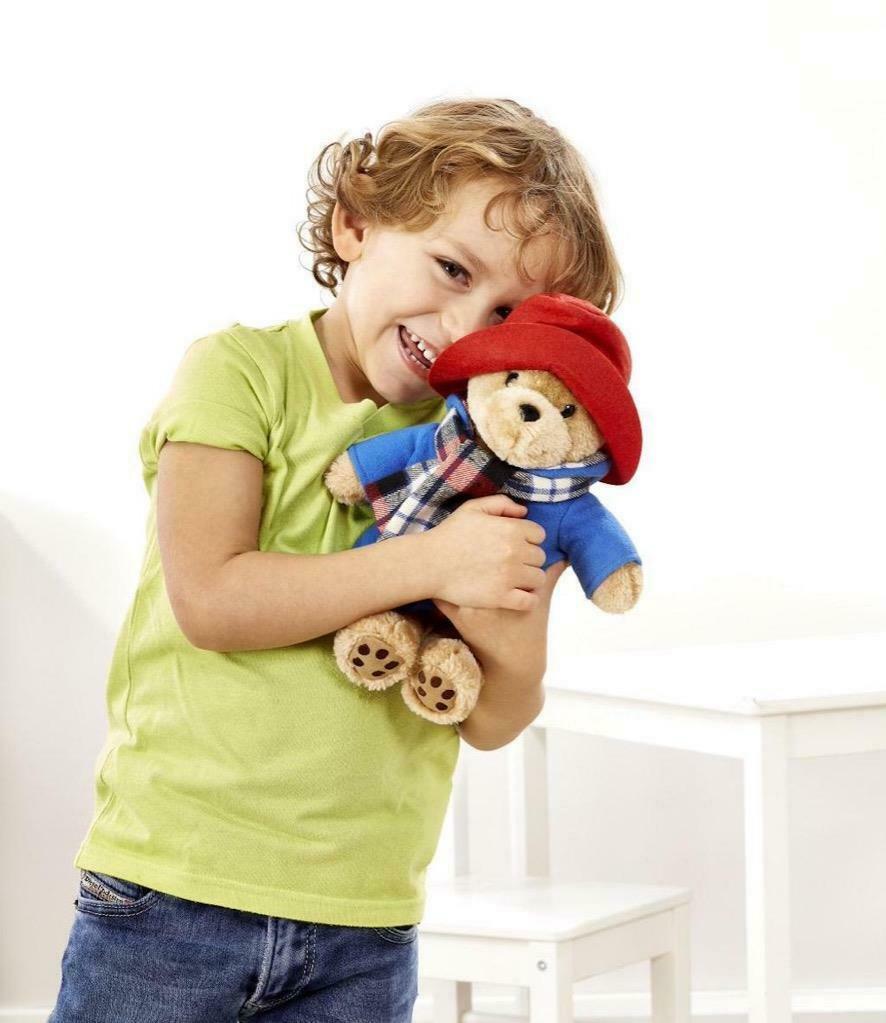 Child holding Anniversary Classic Paddington Bear Christmas gift with his red hat, tartan scarf, blue coat and tag 