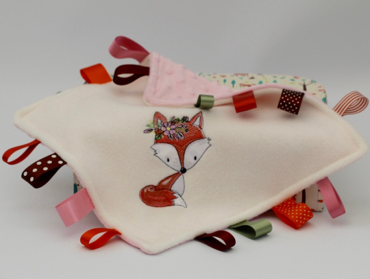 A Floral Fox Taggy Baby Comforter with colourful satin ribbons elevated to show the cute fox