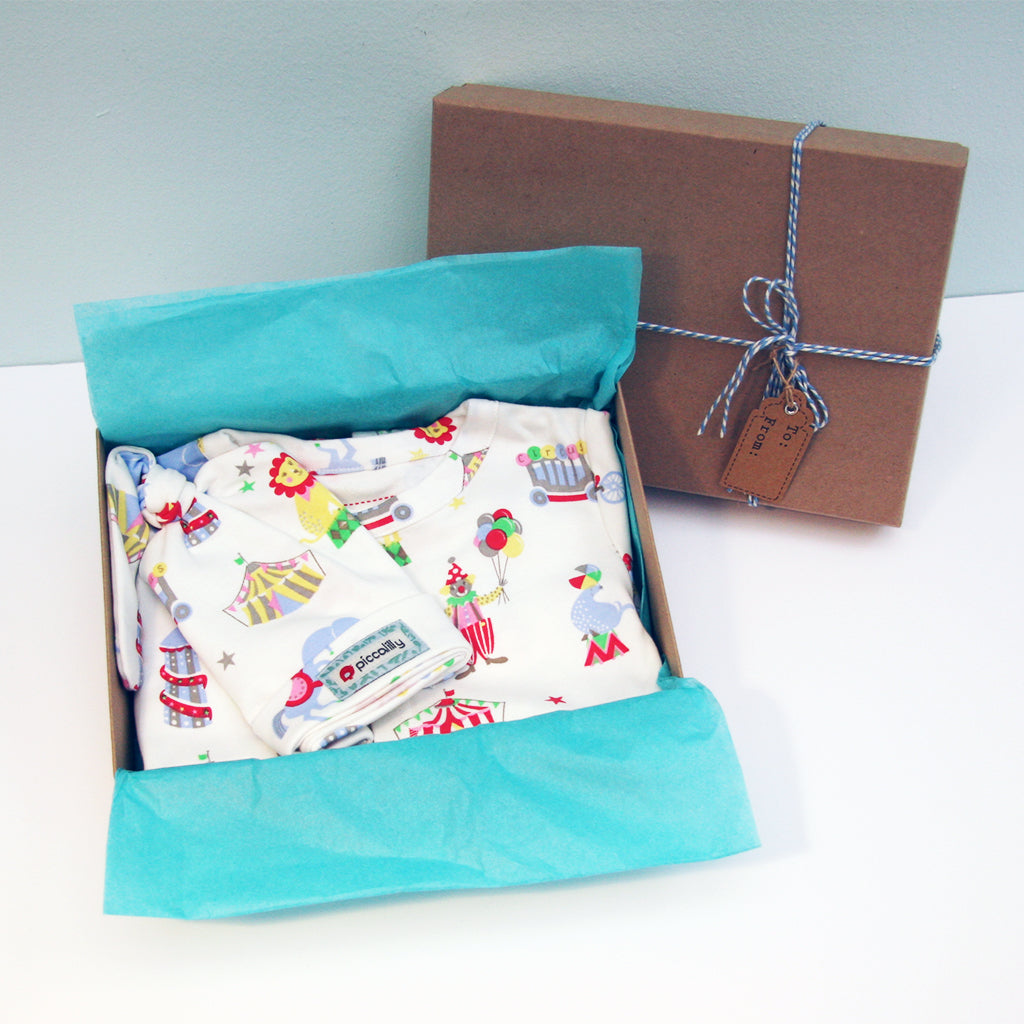 An adorable Gift  Box suitable for a Baby Boy or Baby Girl! A gorgeous Retro Circus footless playsuit & matching knotted hat - features a beautiful circus design from Piccalilly.