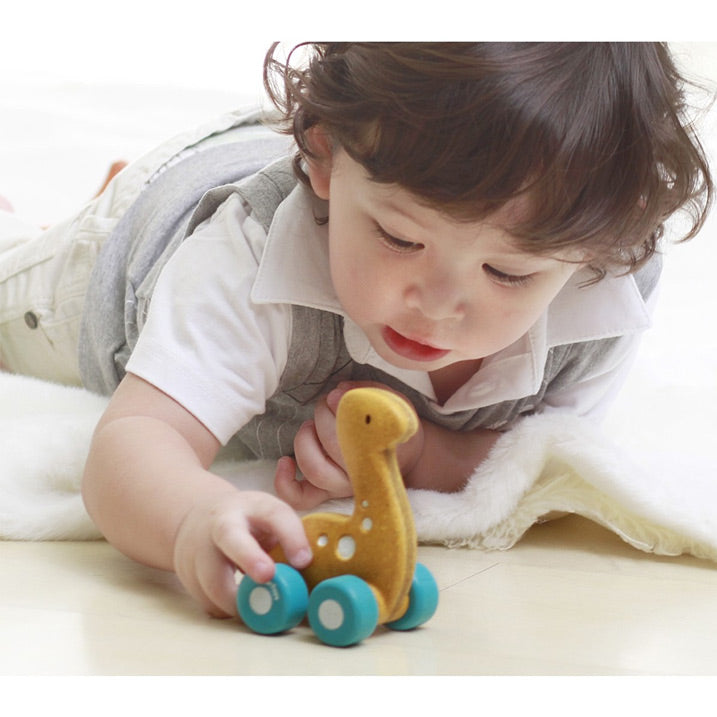Child playing with a Plan Toys Dino Car Rex eco friendly toy for children. Has blue wheels and yellow spots on its body